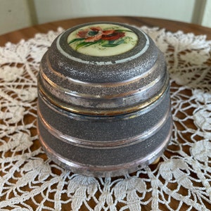 May include: A silver and gold musical jewelry box with a floral design on the lid. The box has a textured surface and is decorated with a gold band around the top.