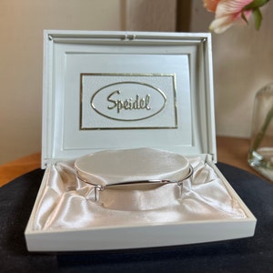 May include: A white box with a satin interior and a silver bracelet. The box has the word "Speidel" printed on the lid.