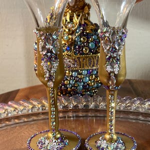 K&ouml;nnte beinhalten: Zwei goldbemalte Schnapsgl&auml;ser mit violetten und klaren Strasssteinen. Die Gl&auml;ser stehen auf einem goldenen Tablett.
