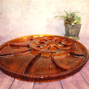 Puede incluir: Una bandeja de servir vintage de vidrio ámbar con seis compartimentos individuales y una sección central con seis cuencos pequeños. La bandeja tiene un borde de cuentas y un diseño floral.