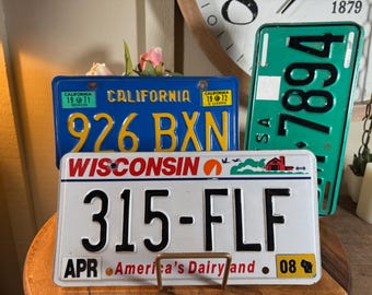 May include: A collection of vintage license plates. A blue California plate with "926 BXN" and a green plate with "7894" are visible. A white Wisconsin plate displays "315-FLF" and "America's Dairy and".
