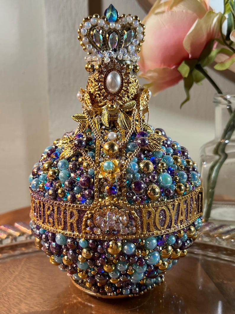 K&ouml;nnte beinhalten: Eine goldene und violette, mit Juwelen besetzte Flasche mit einer Krone oben. Die Flasche ist mit Perlen und Juwelen verziert und tr&auml;gt die Aufschrift "Royal".