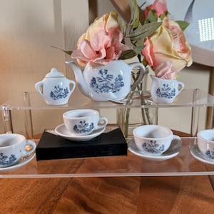 May include: A miniature white porcelain tea set featuring a blue willow pattern. The set includes a teapot, a lidded sugar bowl, a creamer, and four teacups with matching saucers, all decorated with detailed blue landscape illustrations.