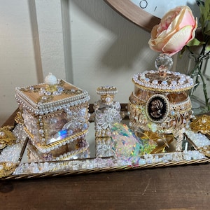 May include: A gold tray with a mirrored surface holds three decorative boxes. The boxes are adorned with pearls, beads, and gold accents. The tray is decorated with gold trim and pearls.