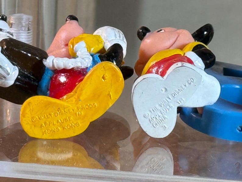 May include: Two vintage Disney character figurines, one featuring Donald Duck and the other Goofy. Donald Duck is wearing a blue shirt, red bow tie, and yellow shoes. Goofy is wearing a red shirt and blue pants. The figurines are marked "Applause" and "Hong Kong" and "China".