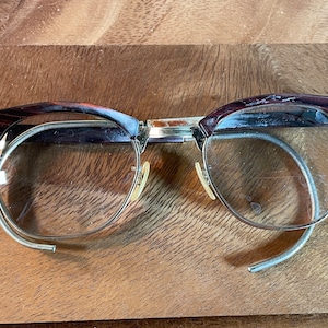 Puede incluir: Gafas vintage de carey con montura de metal dorado y lentes transparentes. Las gafas tienen un estilo clásico y retro.