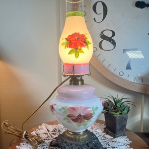 May include: A vintage electric lamp with a white and pink glass base and a clear glass shade with a painted floral design. The lamp has a black metal base with ornate details.