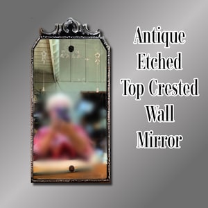May include: A rectangular wall mirror with a dark, ornate metal frame and a decorative top crest. The glass features delicate etched floral patterns near the top. The text "Antique Etched Top Crested Wall Mirror" is displayed to the right.