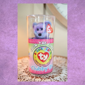 May include: Purple Ty Beanie Baby named Clubby IV in a clear plastic container with a "Join the Club" label. The label features the Ty logo and the words "Beanie Babies Official Club".
