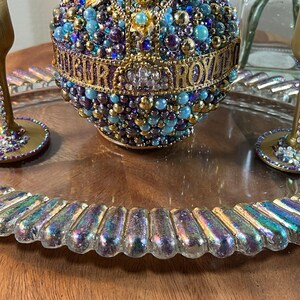 K&ouml;nnte beinhalten: Ein Serviertablett aus Glas mit irisierendem Finish und einem perlenbesetzten, goldverzierten Ornament in der Mitte. Zwei goldbemalte Gl&auml;ser mit Strasssteinen befinden sich auf dem Tablett.