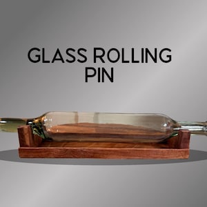 May include: A clear glass rolling pin with a wooden handle and a wooden base. The text "GLASS ROLLING PIN" is displayed above the rolling pin. The rolling pin is resting on a rectangular wooden base.