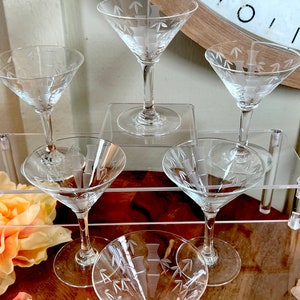 Op de afbeelding: Set van zes heldere glazen martini glazen met gegraveerde bamboe motieven. De glazen zijn gerangschikt op een heldere acryl trapstandaard.