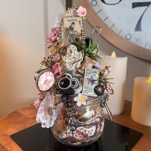 Puede incluir: Un tarro decorativo lleno de adornos de estilo vintage. El tarro presenta un diseño de máquina de coser y está adornado con rosas rosas, un reloj de bolsillo y otras baratijas antiguas. Una pieza única, hecha a mano, con una estética steampunk.