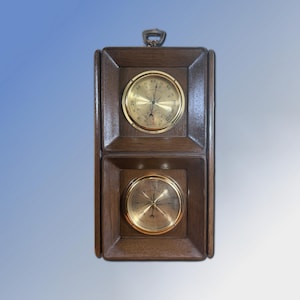 Puede incluir: Una estación meteorológica de madera vintage con dos medidores con caras de latón. El medidor superior muestra la temperatura y el medidor inferior muestra la presión atmosférica. El marco de madera tiene un acabado marrón oscuro y un lazo de metal para colgar.