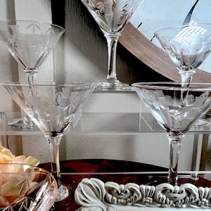 Op de afbeelding: Set van vier heldere glazen martini glazen met gegraveerde ontwerpen op een gelaagde acryl standaard. De glazen zijn gerangschikt in een piramidevorm.