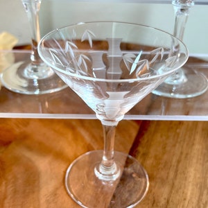 Op de afbeelding: Drie glazen martini glazen met gegraveerde bamboe motieven. De glazen staan op een houten oppervlak.
