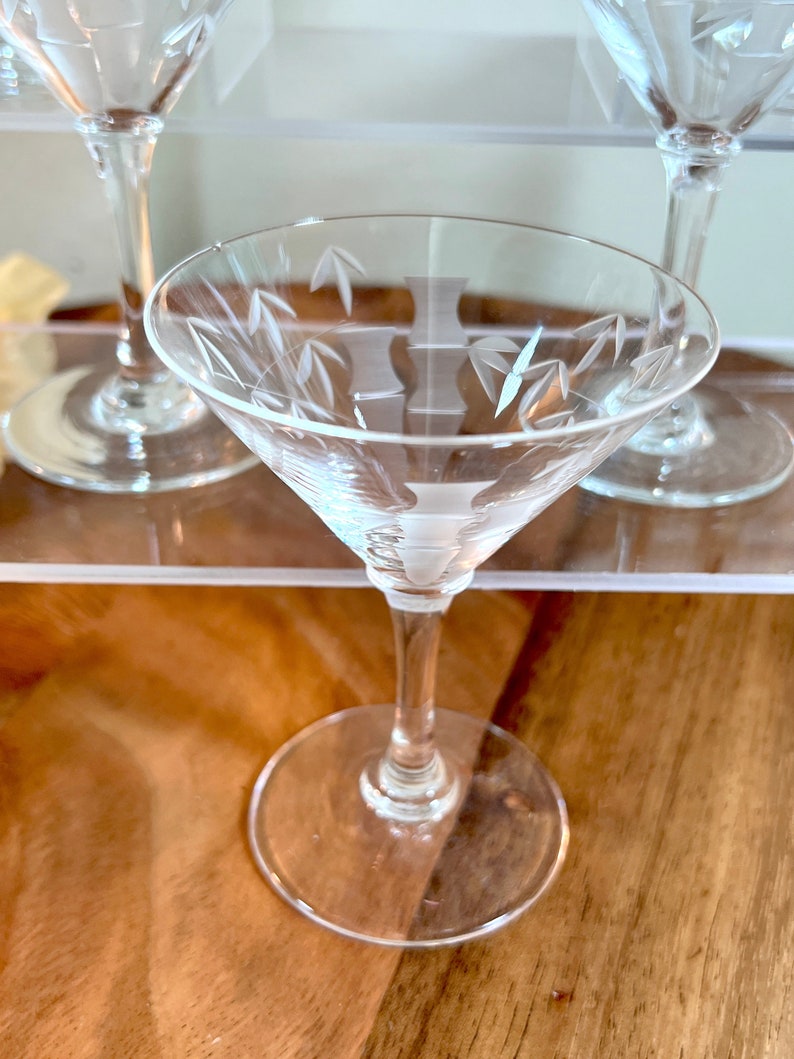 Op de afbeelding: Drie glazen martini glazen met gegraveerde bamboe motieven. De glazen staan op een houten oppervlak.