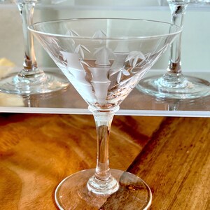 Op de afbeelding: Een helder glazen martini-glas met een gegraveerd ontwerp. Het glas heeft een lange steel en een brede kom.