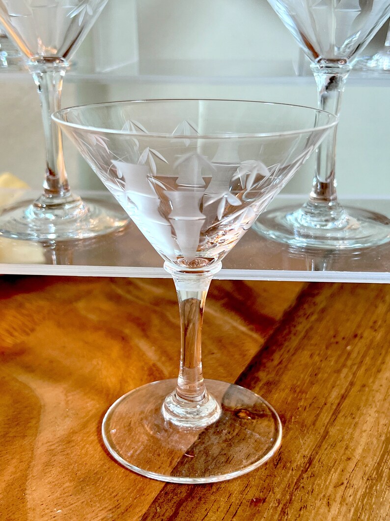 Op de afbeelding: Een helder glazen martini-glas met een gegraveerd ontwerp. Het glas heeft een lange steel en een brede kom.