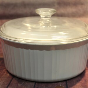 Puede incluir: Plato para hornear de cerámica blanca con tapa de vidrio. El plato tiene un diseño acanalado y un borde dorado.