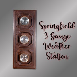 Puede incluir: Una estación meteorológica Springfield 3 Gauge de madera con tres medidores circulares. Los medidores tienen caras plateadas y están colocados en un marco rectangular marrón oscuro con tallas decorativas. El texto "Springfield 3 Gauge Weather Station" está escrito en cursiva.