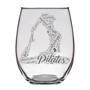 May include: A clear glass wine glass with a design of a person doing a Pilates pose. The design is made up of words related to Pilates, such as "breathing", "control", "strength", and "concentration".