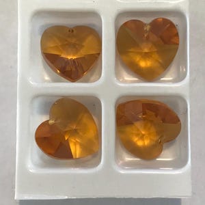 May include: Four amber heart-shaped crystal beads in a white plastic packaging. The beads are arranged in a 2x2 grid.