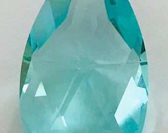 May include: A faceted, teardrop-shaped crystal pendant in a light turquoise color. The pendant has a hole at the top for stringing and is cut with multiple facets to reflect light. The crystal is a decorative element.