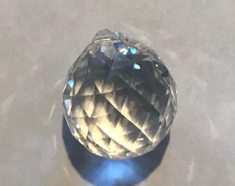 May include: A clear crystal ball with a faceted design. The ball is round and has a smooth surface.