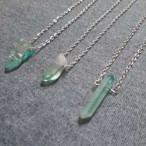 Puede incluir: Tres collares de cadena plateada con colgantes de cristal verde. Los cristales son facetados y tienen un color verde claro.