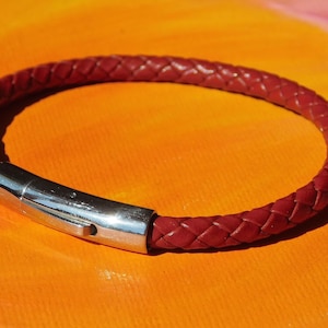 Könnte beinhalten: Ein rotes Lederarmband mit einem silbernen Verschluss. Das Armband ist geflochten und hat ein schlichtes Design.