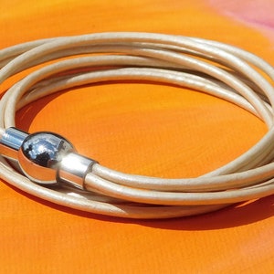 May include: A white leather wrap bracelet with a silver magnetic clasp. The bracelet is made of multiple strands of leather that are woven together.