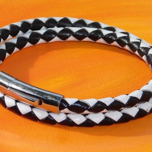 May include: A braided leather bracelet in black and white. The bracelet wraps around twice and has a silver-colored magnetic clasp. The background is a gradient of orange and yellow.
