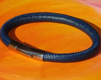 May include: A dark blue leather bracelet with a silver clasp. The bracelet is made of a thick, braided leather and has a simple, elegant design.