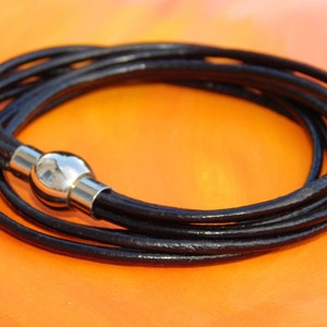 May include: A black leather bracelet with a silver magnetic clasp. The bracelet is made of multiple strands of leather, giving it a layered look.