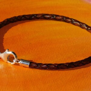 May include: A brown leather bracelet with a silver clasp. The bracelet is braided and has a simple design.