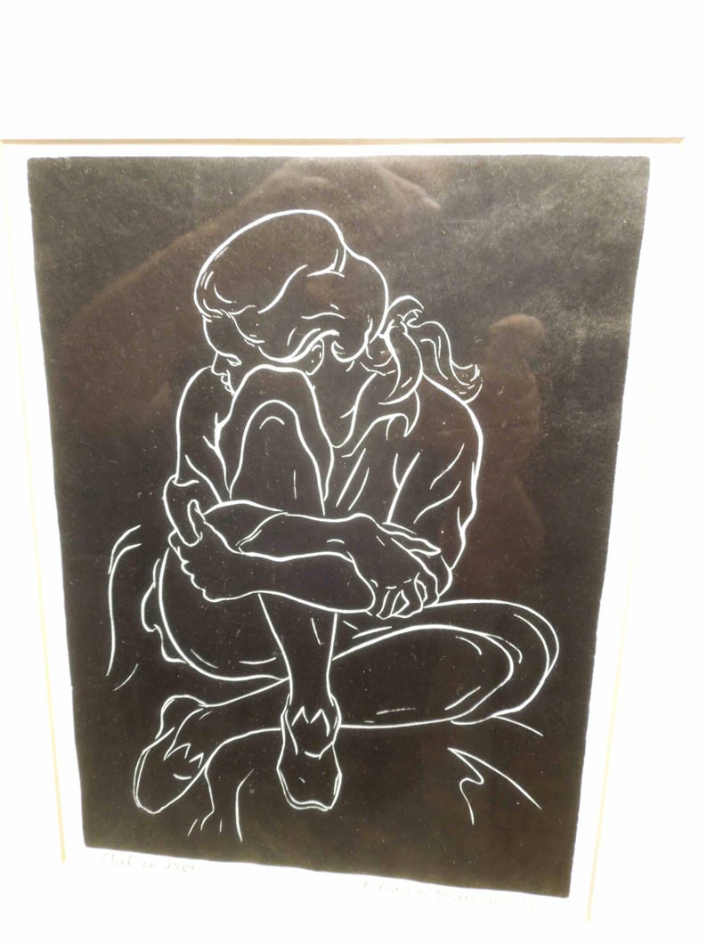 May include: A framed black and white line drawing of a person in a seated position, hugging their knees. The artwork features a minimalist style with white lines against a black background, creating a striking contrast. The person's hair is pulled back in a ponytail.