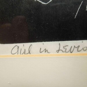 May include: Black and white artwork titled "Girl in Levis". The artwork features a dark, textured background with white line art. The title is handwritten in pencil below the artwork, set against a light-colored background.
