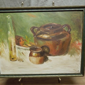 May include: Oil painting of a still life with a brown ceramic pot with handles, a small jar, a bottle, and a plate of food. The painting is in a gold-toned frame and is displayed on a metal easel.