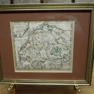 May include: Framed antique map of Norway, featuring detailed cartography with hand-colored green and brown accents. The map is set within a gold-toned frame with a brown mat, displayed on a gold easel.