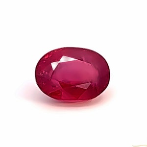 May include: A vibrant red oval-shaped gemstone with a faceted cut. The gemstone is set against a white background.
