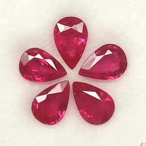 May include: Five vibrant red, pear-cut rubies displayed in a flower arrangement. The gemstones are faceted, reflecting light, and are set against a white backdrop. The image highlights the clarity and colour of the rubies, suitable for jewellery.