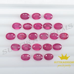 May include: Twenty oval-shaped, pink ruby gemstones. The gemstones are arranged in rows on a white surface. The text "SUTTIKARN GEMS gems for jewellery" is visible in the bottom right corner of the image.