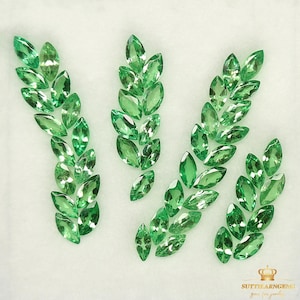 Puede incluir: Una colección de piedras preciosas verdes en forma de marquesa dispuestas en cinco grupos, que se asemejan a hojas. Las piedras preciosas están dispuestas en un patrón simétrico, con cada grupo que contiene aproximadamente 10-15 piedras.
