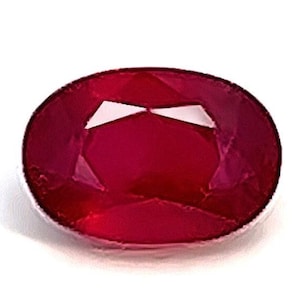 Könnte beinhalten: Ein ovaler Edelstein in tiefroter Farbe mit einem facettierten Schliff.