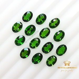 May include: A collection of 12 oval-shaped green gemstones. The gemstones are arranged in rows on a white surface. The gemstones are all approximately the same size and shape.