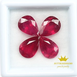 Op de afbeelding: Vier peervormige robijn edelstenen in een witte doos. De robijnen zijn diep rood van kleur en hebben een facetgeslepen vorm. De doos is gevoerd met wit fluweel.