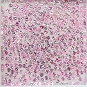 Könnte beinhalten: Nahaufnahme einer großen Menge loser rosa Diamanten. Die Diamanten sind in verschiedenen Größen und auf einer weißen Oberfläche verstreut.