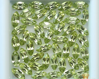 May include: A collection of 50 loose green peridot gemstones in a marquise cut. The gemstones are displayed in a white square box.
