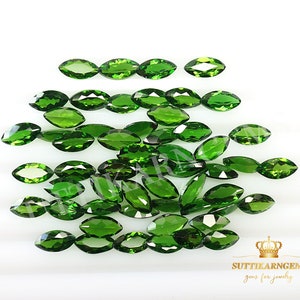 May include: A collection of 25 marquise-shaped green gemstones. The gemstones are arranged in a loose pile on a white surface.